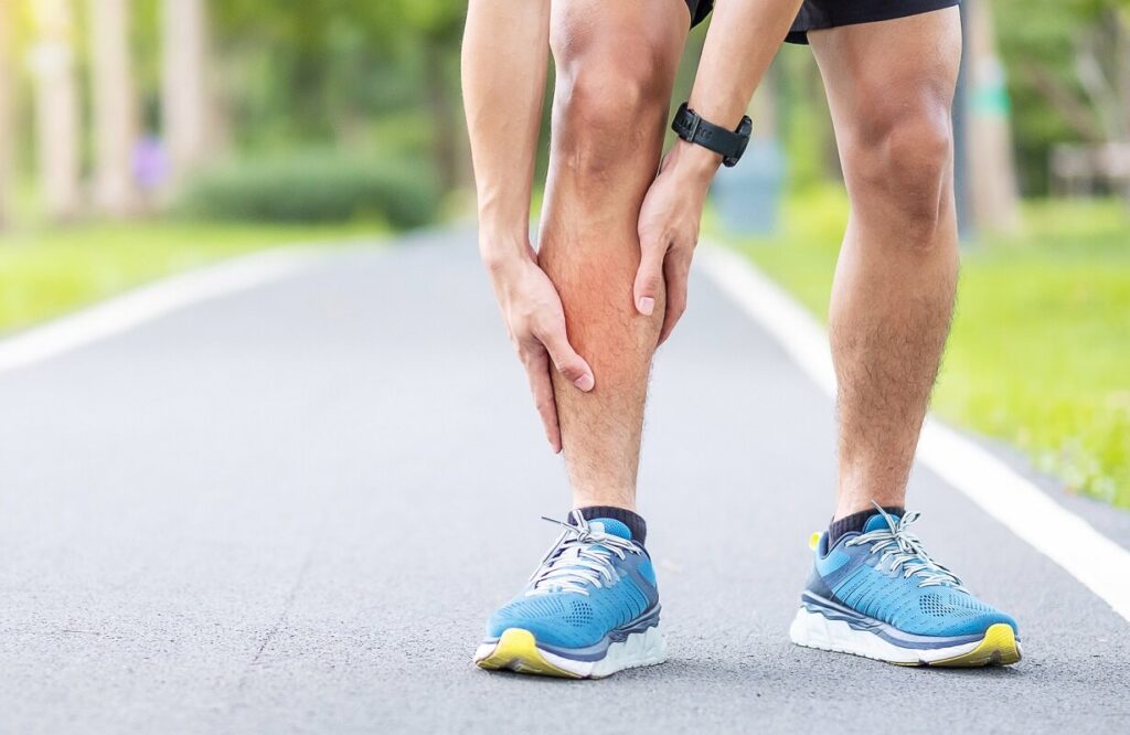Young adult male with his muscle pain during running. Runner having leg ache due to Shin Splints. Sports injuries and medical concept