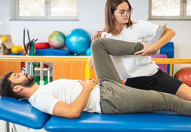 A female physiotherapist is holding the leg of a male patient doing manual therapy/stretching to help his hip move better.