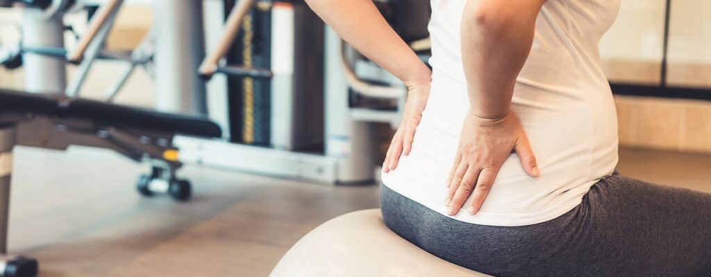 pregnant woman sits on an exercise ball with her hands on her low back